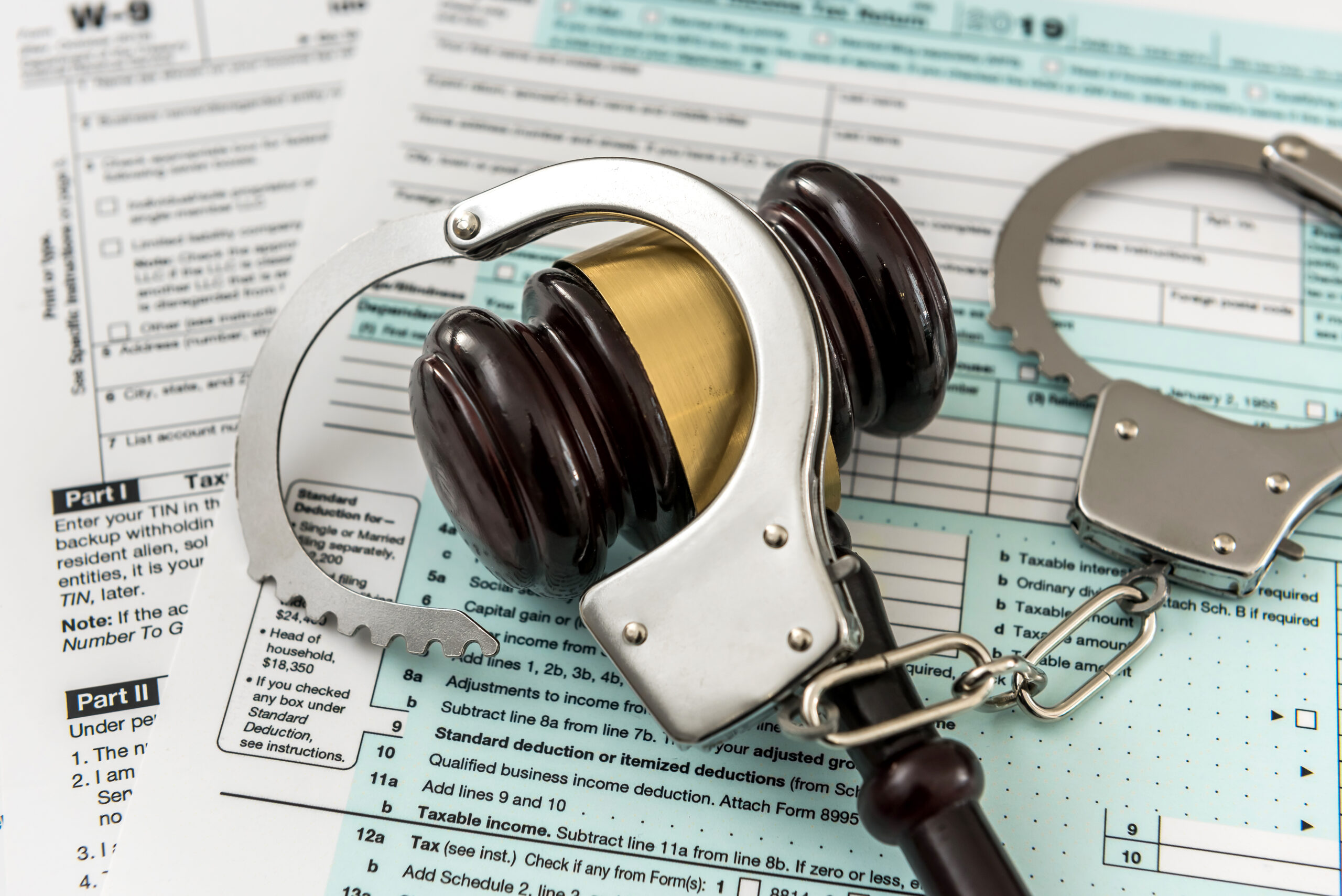Wooden gavel with handcuff lying on tax form. Time for tax, illegal concept
